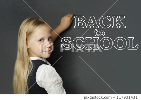 Blonde little girl child elementary student writing Back to school inscription  117931431