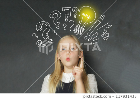 Smart child girl student with yellow light bulb and question marks on school blackboard background.  117931433