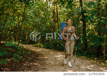 A woman enjoys trekking in a beautiful lush forest with a backpack and trekking poles 117931850