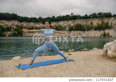 A Woman Engaging in Yoga Practice by the Peaceful and Serene Lake Surrounded by Nature A Woman Engaging in Yoga Practice by the Peaceful and Serene Lake Surrounded by Nature 117931887