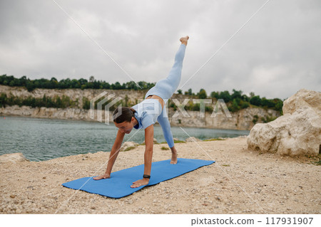 Yoga Pose by the Water Performing a Handstand while Elevating One Leg for Balance and Stability Yoga Pose by the Water Performing a Handstand while Elevating One Leg for Balance and Stability 117931907