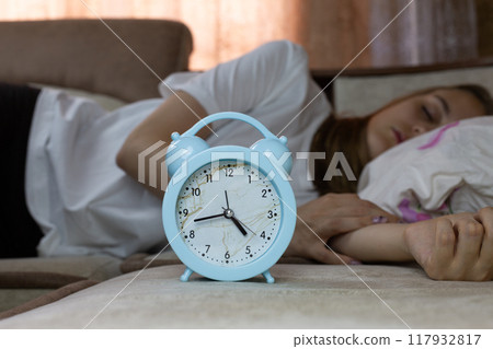 Home alarm clock on sofa with young woman sleeping at home after hard day, healthy daytime sleep Home alarm clock on sofa with young woman sleeping at home after hard day, healthy daytime sleep 117932817