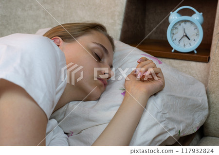 Young woman sleeping on pillow at home next to alarm clock to wake her up after nap, lazy girl sleeping on sofa 117932824