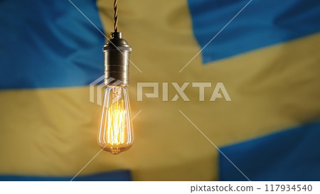 Glowing Edison light bulb on swedish flag background. Electricity price, bills, energy crisis 117934540