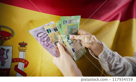 Spanish flag background. Woman counting money euros. Credits, raising tariffs in EU Europe 117934559