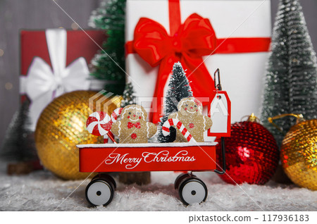 Merry Christmas and Happy New Year greeting card. Gingerbread men and lollipops in a cart on background of New Year gifts and Christmas tree balls. Merry Christmas and Happy New Year greeting card. Gingerbread men and lollipops in a cart on background of New Year gifts and Christmas tree balls. 117936183