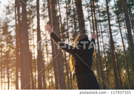 teen girl raised hands from behind in winter pine forest in sunset teen girl raised hands from behind in winter pine forest in sunset 117937103