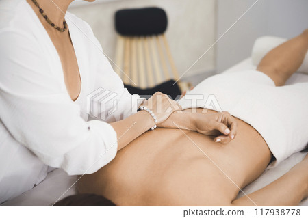 Process of back massage in pro salon. Hands of female therapist on a body of a woman laying face down on massage table, close-up, selective focus. 117938778