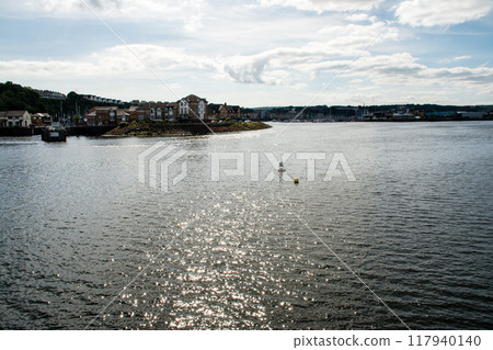 南威爾斯的一個令人眼花繚亂的海灣，陽光反射在水面上，遠處可見遊艇港口和磚砌建築 117940140