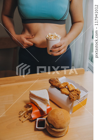 To eat or not. Cheerless plump woman looking at the burger while thinking to eat it or not To eat or not. Cheerless plump woman looking at the burger while thinking to eat it or not 117941012