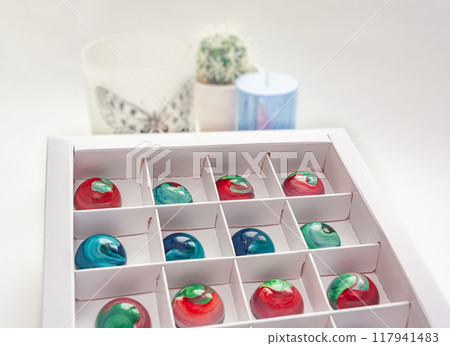 Tempered chocolate candies with glossy painted body in a box with blurred background and bokeh elements 117941483