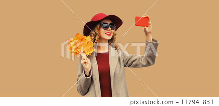 Autumn portrait of stylish happy smiling young woman taking selfie with phone holding yellow leaves Autumn portrait of stylish happy smiling young woman taking selfie with phone holding yellow leaves 117941831