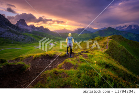 Woman with backpack and beautiful alpine mountain peaks at sunse Woman with backpack and beautiful alpine mountain peaks at sunse 117942045