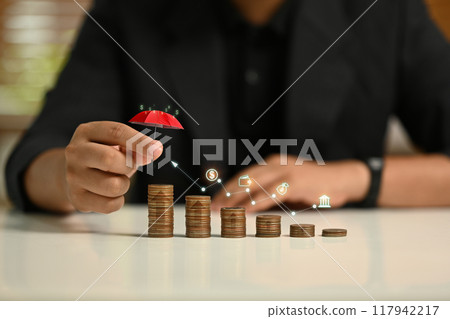 Man holding a small red umbrella over a stack of coins, symbolizing financial protection and savings concept 117942217