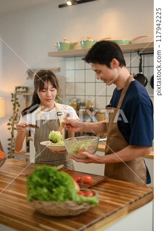 Young couple wearing aprons enjoying their cooking time in a modern kitchen. Healthy and nutritious lifestyle concept 117942225