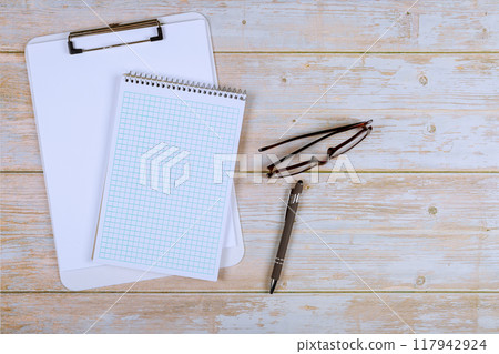 In modern office, notebook, glasses, pen can be seen on table for work In modern office, notebook, glasses, pen can be seen on table for work 117942924
