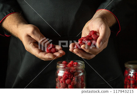 Close-up of a cook hands filling a jar with ripe raspberries. Concept of making raspberry jam or sweet drink. Rubus idaeus canning Close-up of a cook hands filling a jar with ripe raspberries. Concept of making raspberry jam or sweet drink. Rubus idaeus canning 117943215