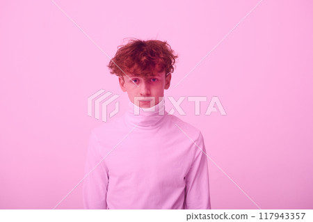 Portrait of a young man looking straight at camera, wearing high-neck sweater against pink background. His curly hair and serious expression are highlighted by soft lighting Portrait of a young man looking straight at camera, wearing high-neck sweater against pink background. His curly hair and serious expression are highlighted by soft lighting 117943357