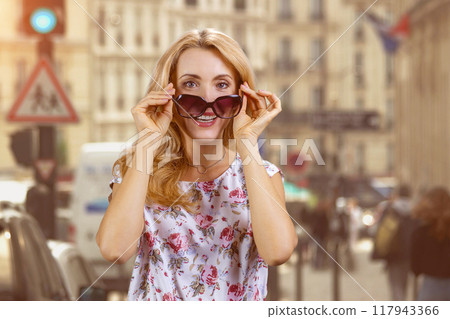 Portrait of happy mature woman standing outdoors with sunglasses. Urban city street in the background. 117943366