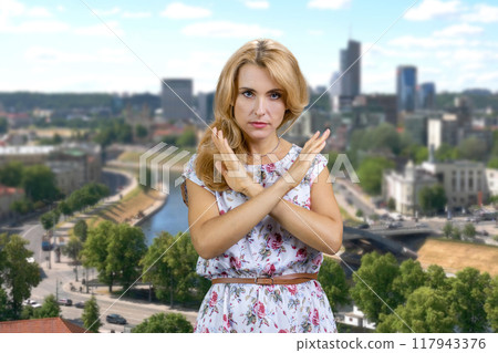 Portrait of sad negative woman show stop gesture sign cross her arms. Summer cityscape in the background. 117943376
