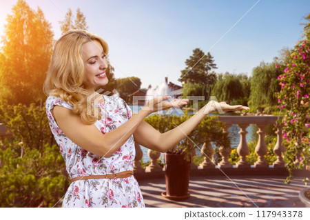 Portrait of a blonde mature woman advertising copy space with both hands in the park. Green summer landscape in the background. Portrait of a blonde mature woman advertising copy space with both hands in the park. Green summer landscape in the background. 117943378