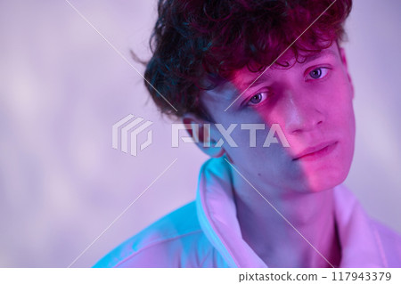 Portrait of young man looking straight at camera with a contemplative expression while bathed in colorful lighting creating an artistic and modern look Portrait of young man looking straight at camera with a contemplative expression while bathed in colorful lighting creating an artistic and modern look 117943379