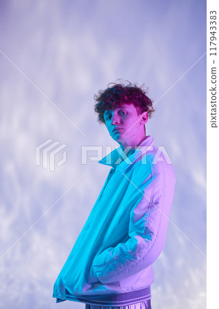 Young man posing against gradient background with soft pastel lighting enveloping subject creating a dreamy effect while wearing casual jacket and relaxed posture Young man posing against gradient background with soft pastel lighting enveloping subject creating a dreamy effect while wearing casual jacket and relaxed posture 117943383