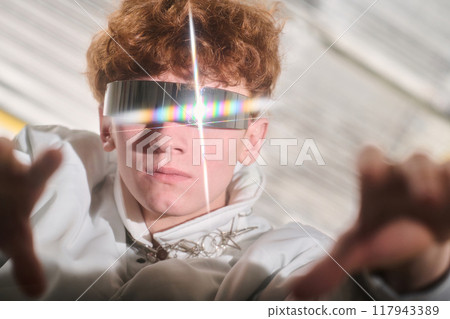 Portrait of someone wearing futuristic reflective glasses with outstretched hands and a white outfit standing in a well-lit space with a focused expression Portrait of someone wearing futuristic reflective glasses with outstretched hands and a white outfit standing in a well-lit space with a focused expression 117943389