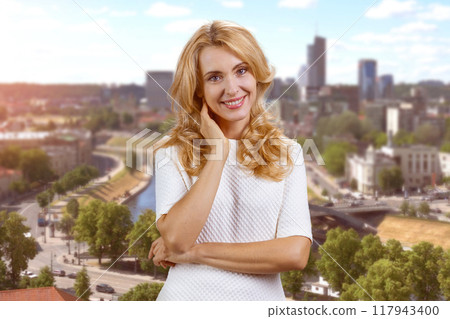 Portrait of happy charming mature blonde woman outdoors. Urban cityscape in the background. 117943400