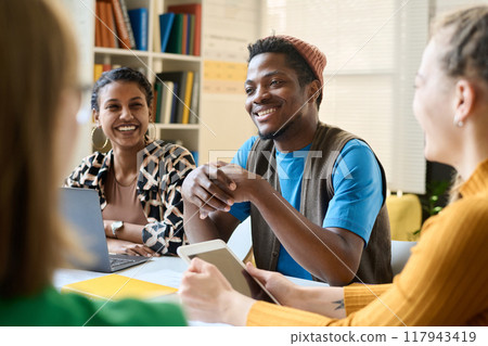 Portrait of Black young student smiling while sitting at table and working together during class in school or college 117943419