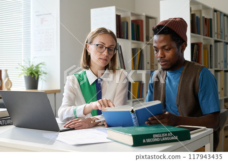 Black young man as student having personal class in school or college with teacher and using laptop together in library 117943435