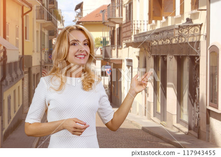 Happy cheerfyl blonde woman pointing at copy space. European street in the background. Happy cheerfyl blonde woman pointing at copy space. European street in the background. 117943455