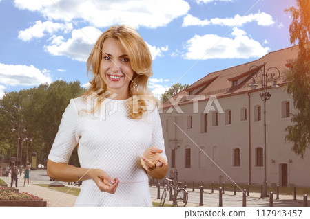 Portrait of cheerful blonde mature woman talking you you and gesturing. Urban city street and buildings in the background. Portrait of cheerful blonde mature woman talking you you and gesturing. Urban city street and buildings in the background. 117943457