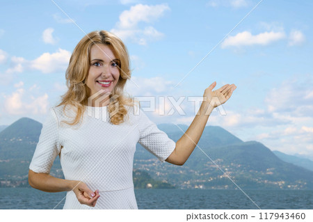 Happy mature blonde woman pointing at nature landscape. Mountain scenery in the background. 117943460