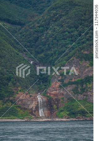 A cliff-like mountainside with a waterfall in sight 117944036