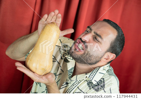 Funny young adult man with white shirt playing with Pumpkin and biting it Funny young adult man with white shirt playing with Pumpkin and biting it 117944431