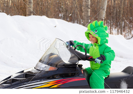 Boy is on a snowmobile in a snowy park in dragon-like outwear. 117946432