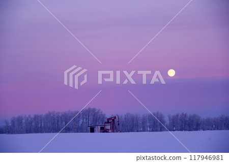 Winter landscape in prairies - field along the forest covered with snow and the pump jack in the center extracting oil, full moon in the sky Winter landscape in prairies - field along the forest covered with snow and the pump jack in the center extracting oil, full moon in the sky 117946981