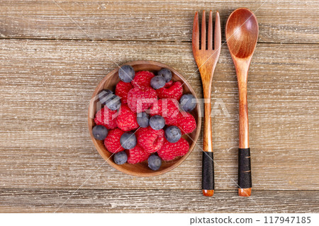 Mix of blueberries and raspberries in a plate with wooden fork and spoon. 117947185