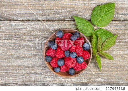 Plate with raspberries and blueberries with leaves on the wooden rustic table. Plate with raspberries and blueberries with leaves on the wooden rustic table. 117947186