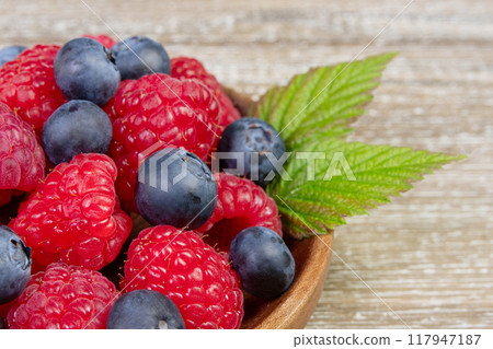 Plate with raspberries and blueberries with leaves on the wooden rustic table. Plate with raspberries and blueberries with leaves on the wooden rustic table. 117947187