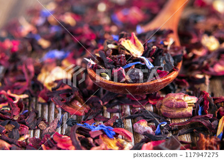 Tea mix of karkade, flowers and berries in a spoon and on the table. Tea mix of karkade, flowers and berries in a spoon and on the table. 117947275