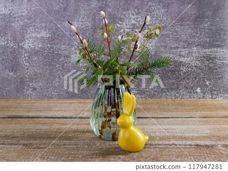 Figurine of yellow Easter bunny and a bunch of branches on the table. Figurine of yellow Easter bunny and a bunch of branches on the table. 117947281