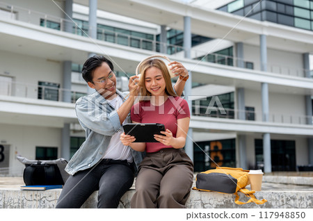 A caring Asian man is placing headphones on his girlfriend while she looks at a tablet. 117948850