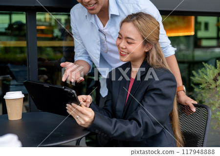 Two positive Asian colleagues are discussing work, having an informal meeting at a coffee shop. 117948888