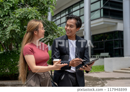 A positive Asian businessman is briefing his assistant on work while walking outdoors. A positive Asian businessman is briefing his assistant on work while walking outdoors. 117948899