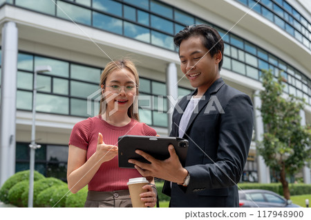 A beautiful Asian female assistant is discussing work with her boss while walking outdoors. 117948900