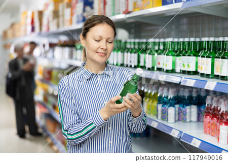 Woman customer is thinking about buying spicy and unusual Korean soy wine chum churum. 117949016