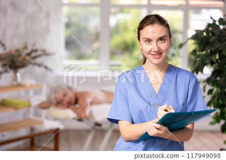 Young woman physiotherapist writes down and enters patients data into medical card. 117949098