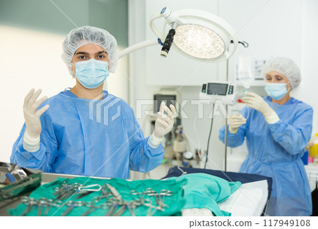 Man doctor stand with raised hands in gloves, female assistant pushes dropper system, medications Man doctor stand with raised hands in gloves, female assistant pushes dropper system, medications 117949108